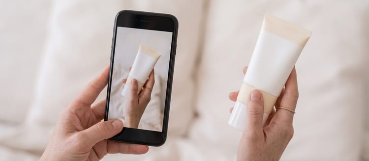 Hands photographing a skincare tube on a phone